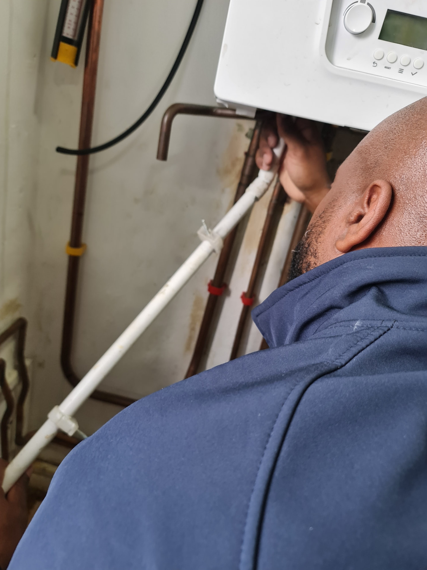 Teon, Gas Safe registered engineer, working on the pipework beneath a wall-mounted boiler
